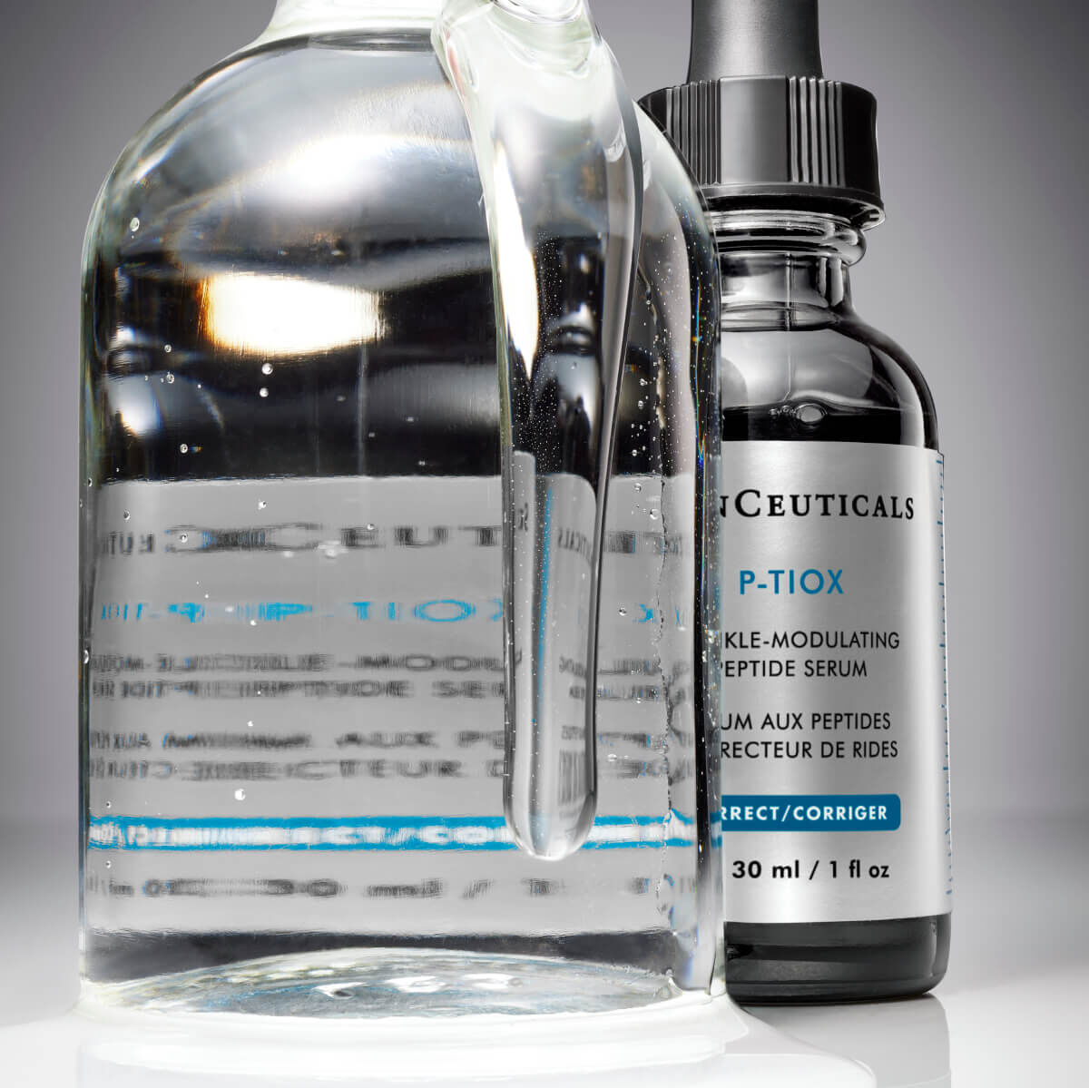 A glass bottle filled with clear liquid beside a dark serum bottle, both labelled with skincare product details.
