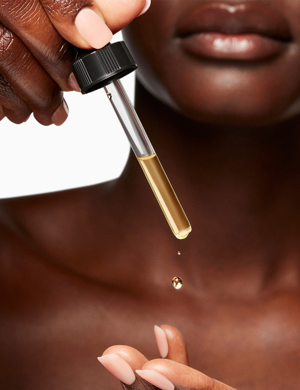 A woman’s hand delicately holds a dropper, dispensing a golden serum onto her fingertips