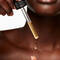 A woman’s hand delicately holds a dropper, dispensing a golden serum onto her fingertips