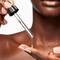 A person's hand delicately holds a dropper, dispensing a clear serum onto their fingertips