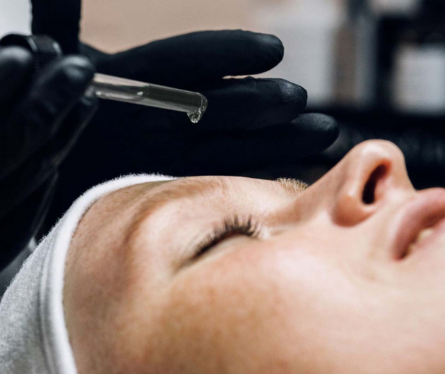 A close-up of a woman receiving a facial treatment, with a professional applying serum from a dropper.
