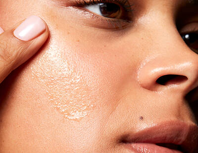 Close-up of a person applying a skincare product to their cheek, highlighting smooth, glowy skin and a natural beauty look.