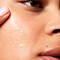 Close-up of a person applying a skincare product to their cheek, highlighting smooth, glowy skin and a natural beauty look.