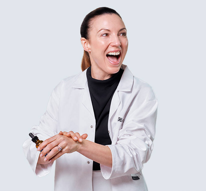 Dr. Emma Craythorne smiling whilst holding a SkinCeuticals antioxidant serum and pressing the formulation into the back of her hand