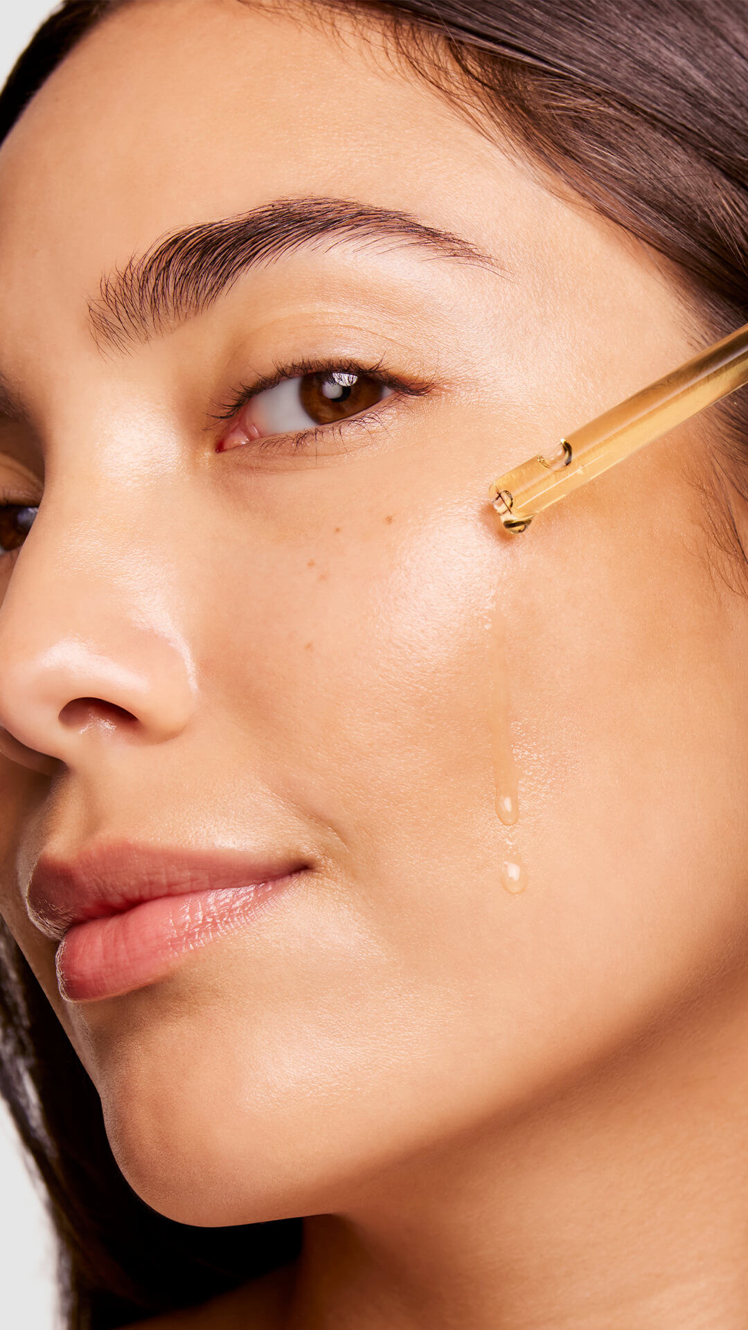 A close-up of a woman applying a clear serum to her cheek, highlighting her glowing skin and natural beauty.