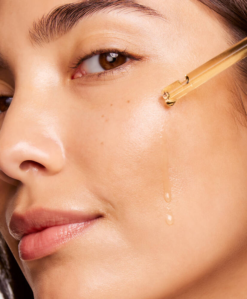 A close-up of a woman applying a clear serum to her cheek, highlighting her glowing skin and natural beauty.