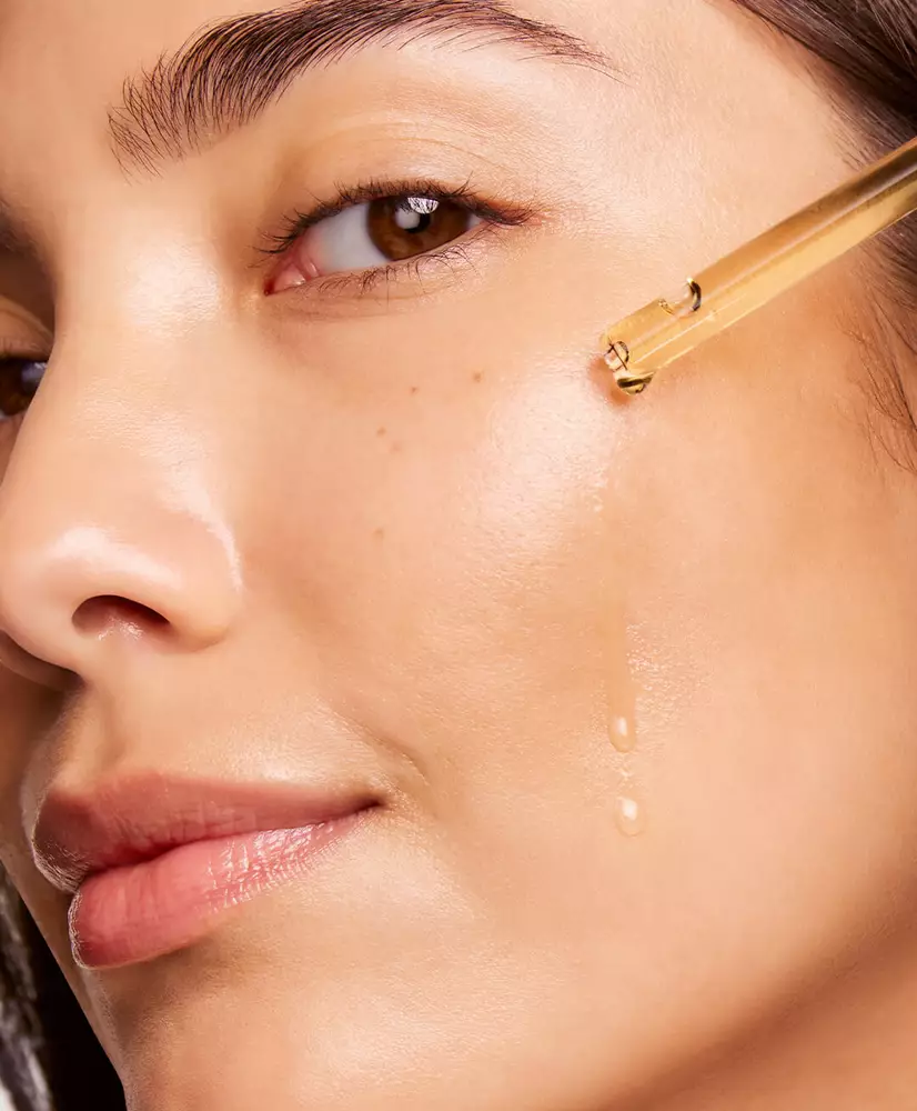 A close-up of a woman applying a clear serum to her cheek, highlighting her glowing skin and natural beauty.