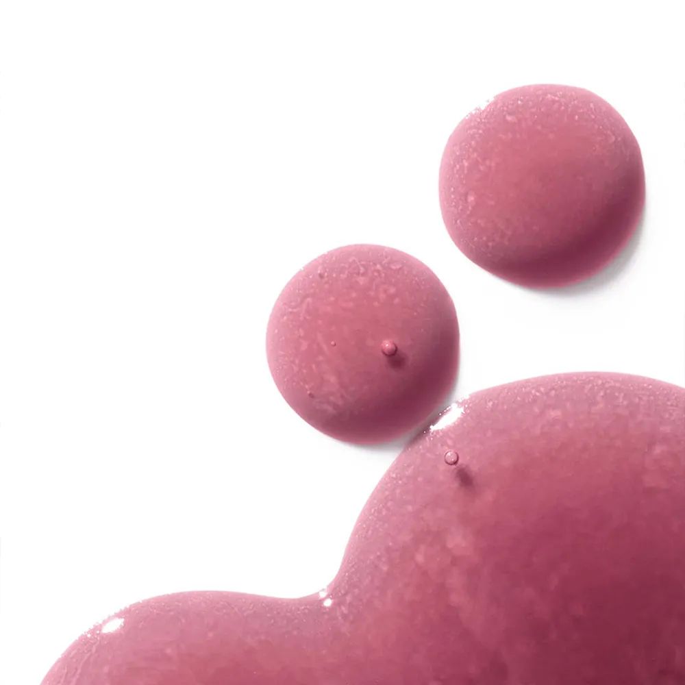 Circular drops of a raspberry pink skincare serum on a white background